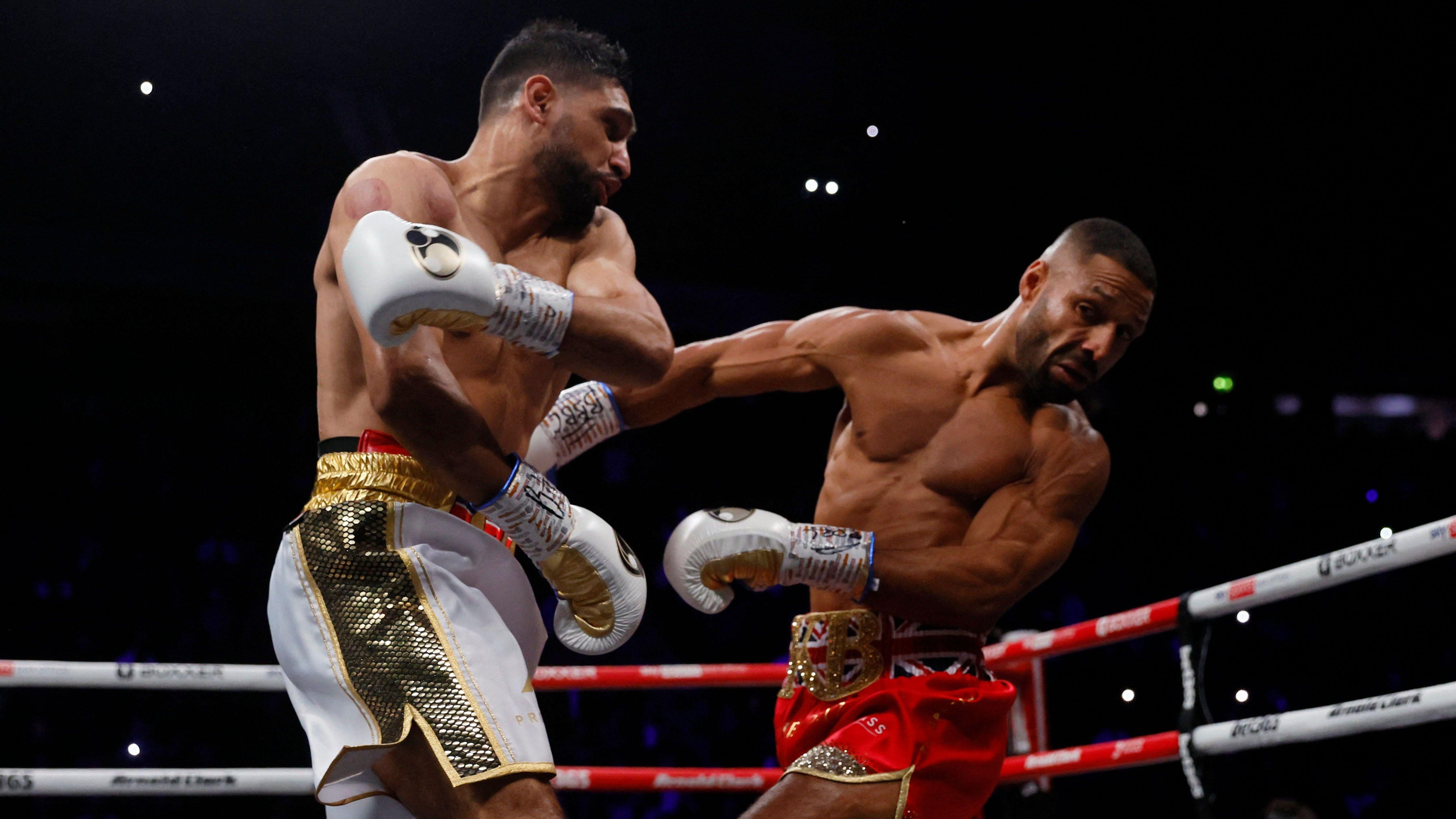 Amir Khan (left) and Kell Brook (right) exchange punches during a professional boxing match. Khan, wearing white and gold shorts and white boxing gloves.