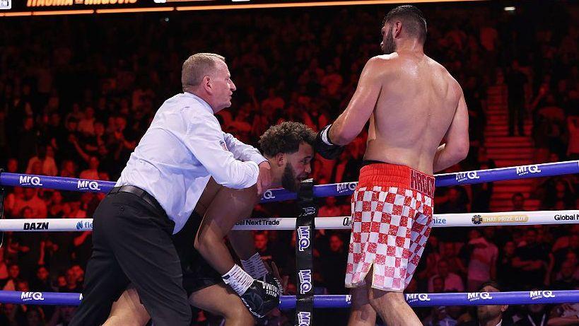 Moses Itauma is held on the ropes by the referee as Filip Hrgovic watches
