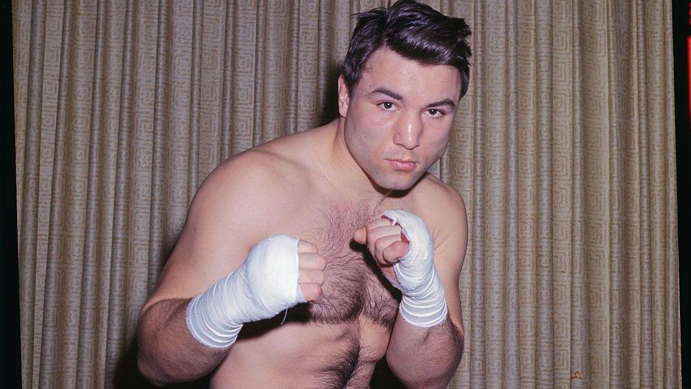 Chuvalo as a young man, shirtless and wearing boxing shorts, holding up his fists in punching pose