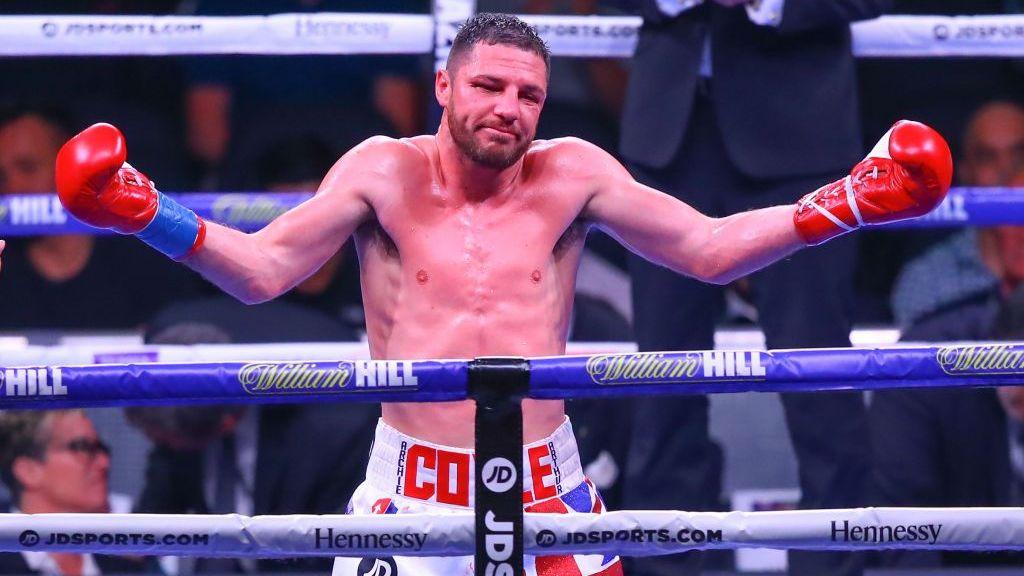 An image taken in the past of Tommy Coyle. He's mid boxing match with red gloves on and shorts saying Coyle in red writing. He's stood at the edge of a large boxing ring.