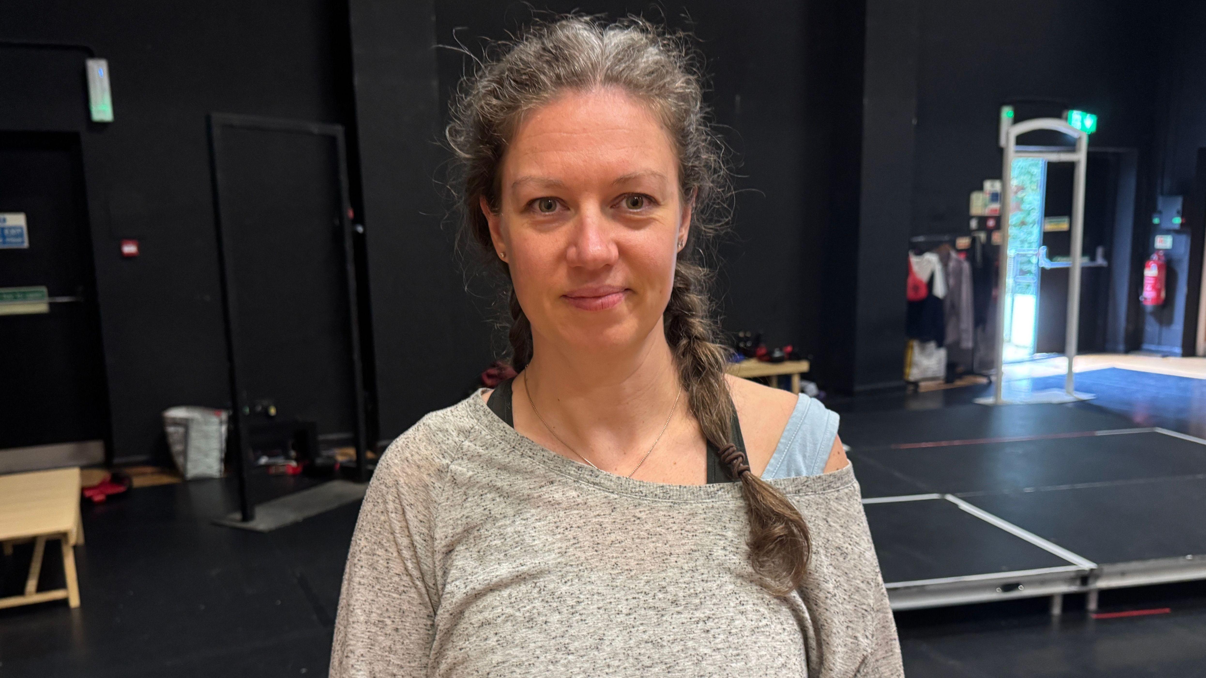 A lady wearing a grey long sleeved t-shirt. She is looking straight ahead.