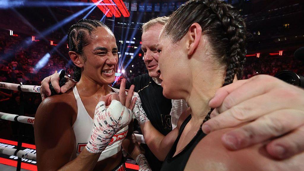 Amanda Serrano holds up three fingers as she embraces Katie Taylor in a boxing ring